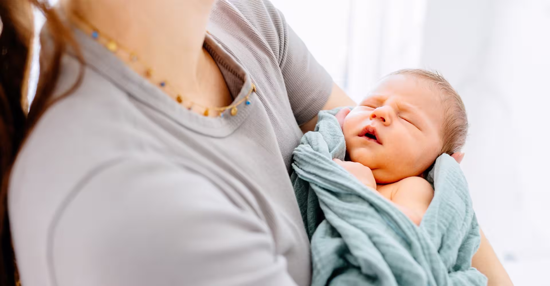 newborn baby sleeping in mother's arms wrapped in a blanket